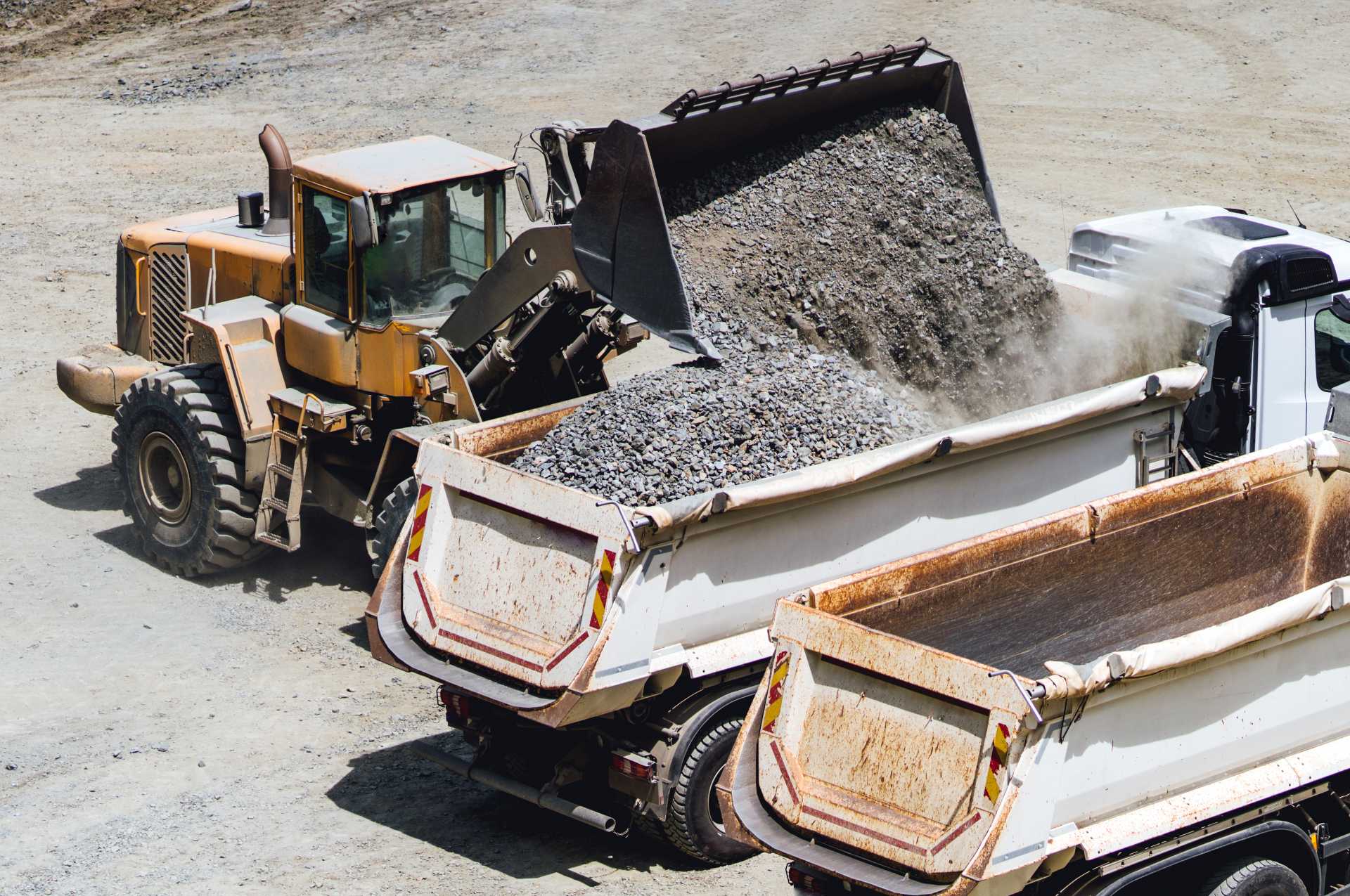 aggregate transportation cost, a wheel loader sumping gravel in trucks on a construction site.